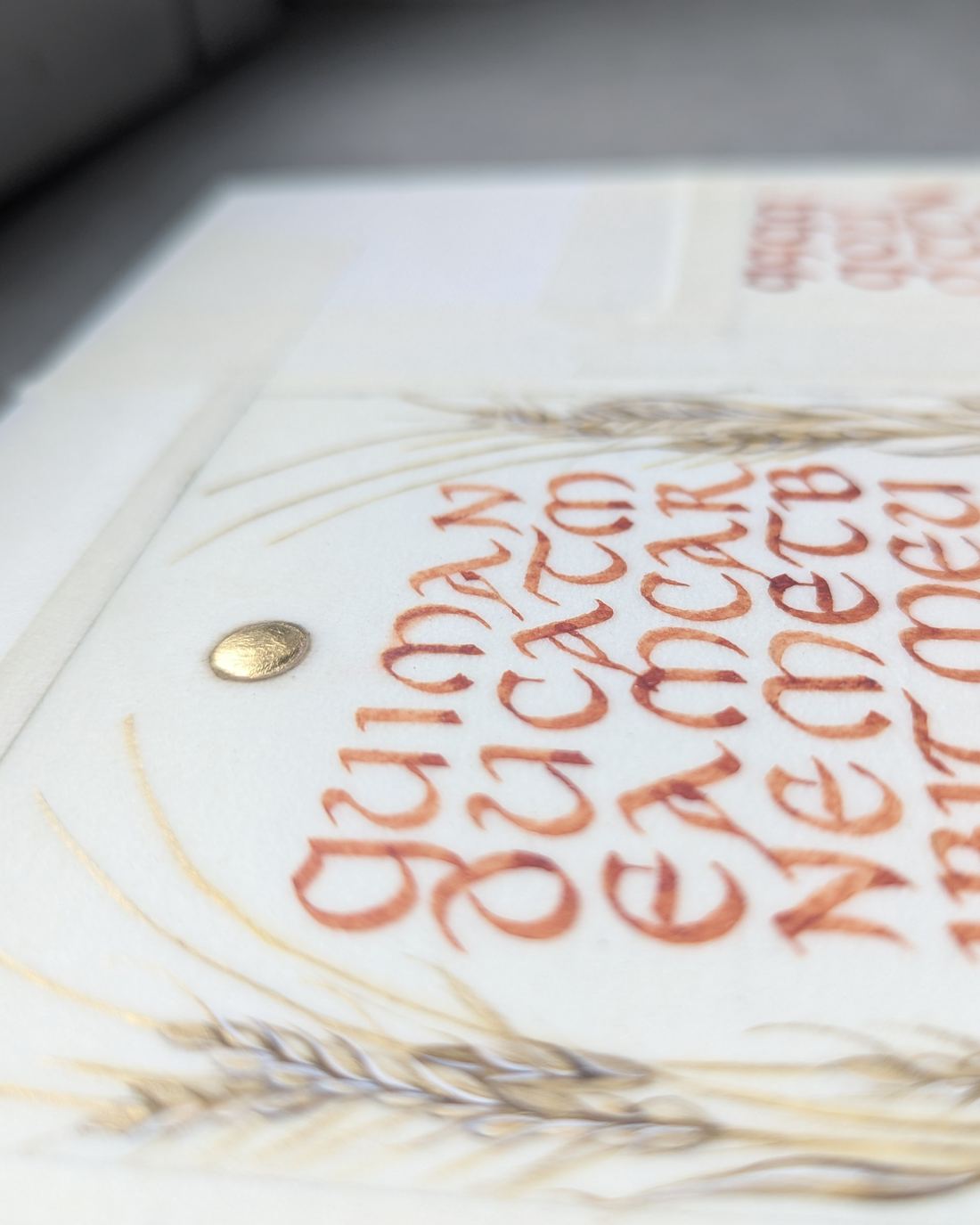 Une calligraphie aux encres ocre, entourée d’épis de blé peints, rehaussée d’un point d’or sur le parchemin
